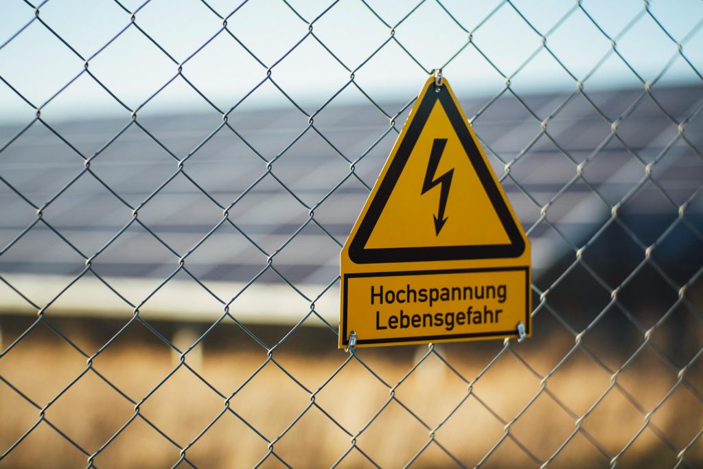 Warning sign indicating high voltage danger on a chain link fence near solar panels.