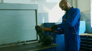 A technician in overalls using a grinder on metal in an industrial workshop.