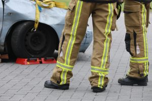 Firefighters inspecting a car accident wearing protective gear. Focus on pants and footwear.