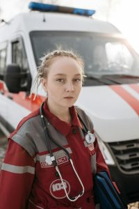 Female paramedic in uniform standing by an ambulance, looking focused and ready for action.
