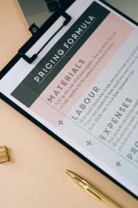 Close-up of a clipboard showcasing a pricing formula with a pen on the desk.